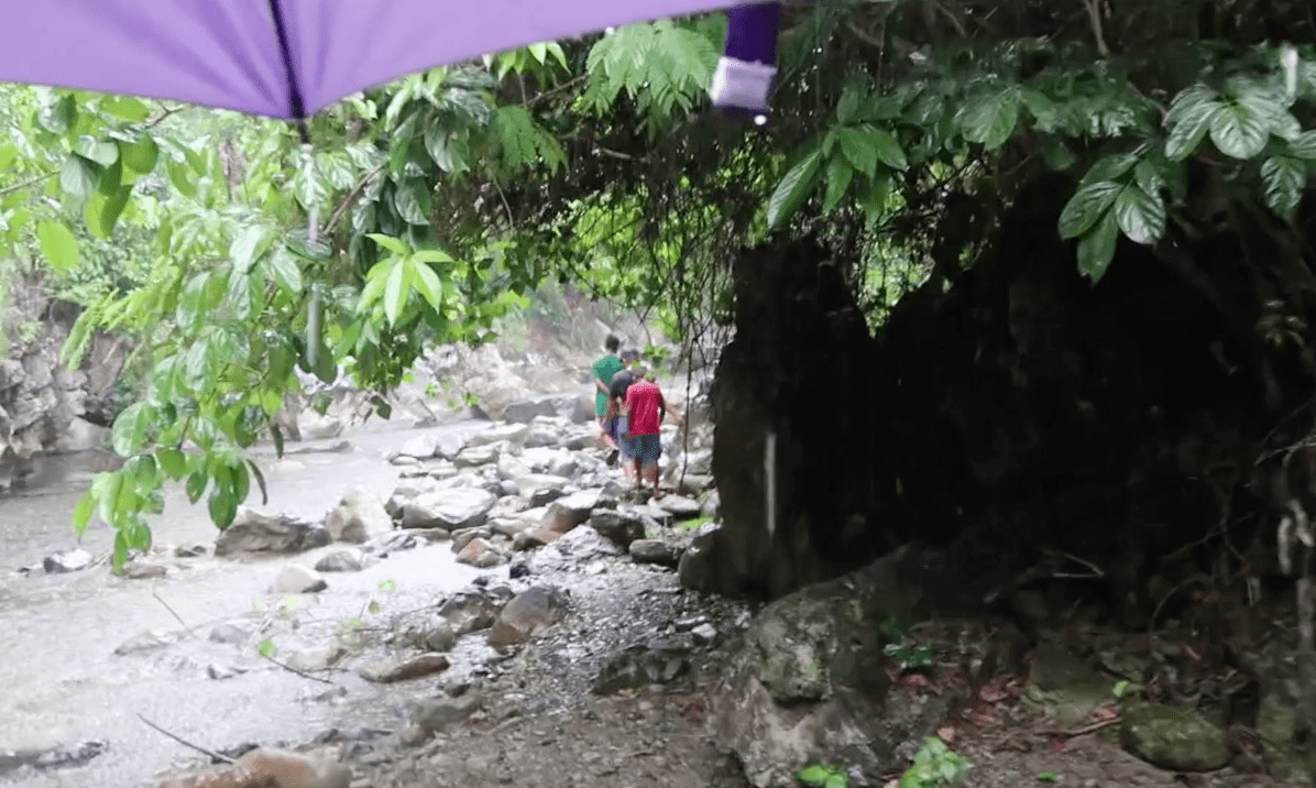 seeing filipino locals walking through the rain at a rocky riverside in the catanduanes province philippines